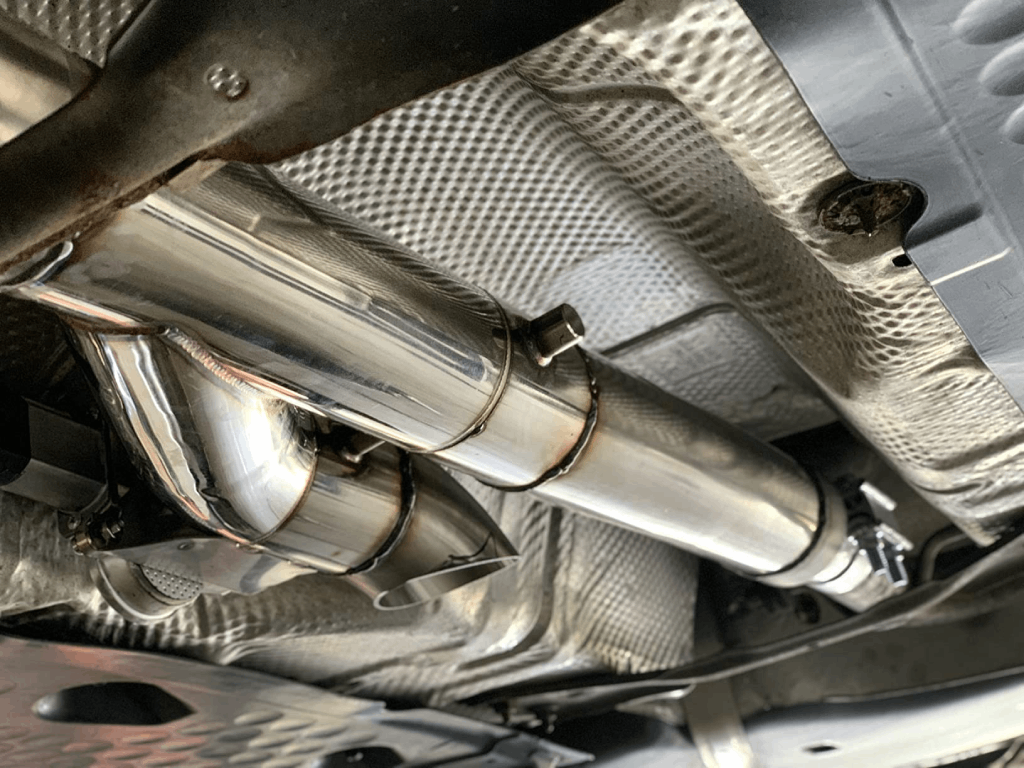 Exhaust cutout welded into the factory exhaust underneath a vehicle, routed past the heat shield